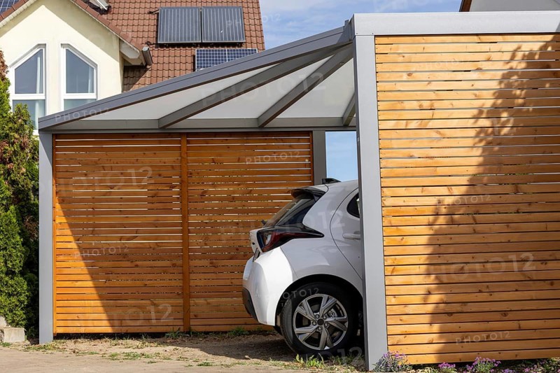 Beautiful carport made of wood and metal with side slatted walls and a fixed roof next to a residential building