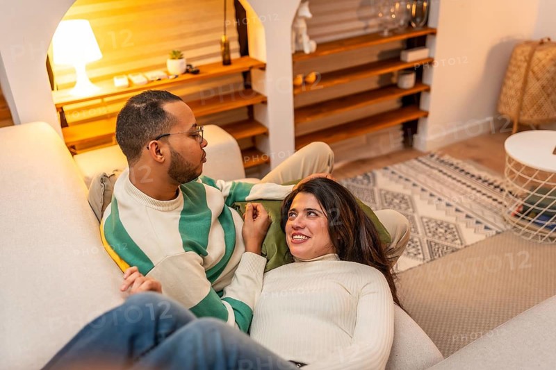 Young couple enjoying a cozy moment on the living room sofa, with the woman resting on the man's lap, sharing an affectionate and intimate connection in their home