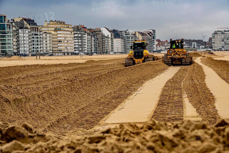 Bulldozers when distributing sand on the beach in the town of Knokke-Heist, part of coastal protection and beach maintenance, due to floods, erosion and sea level rise, the sand on the beach is repeatedly washed into the sea, in winter the sand from the seabed is washed back onto the beach with suction vessels, the excavators and levelers then distribute the sand back on the beach to eliminate the difference in height so as to bathe To make the beach usable again for the next season