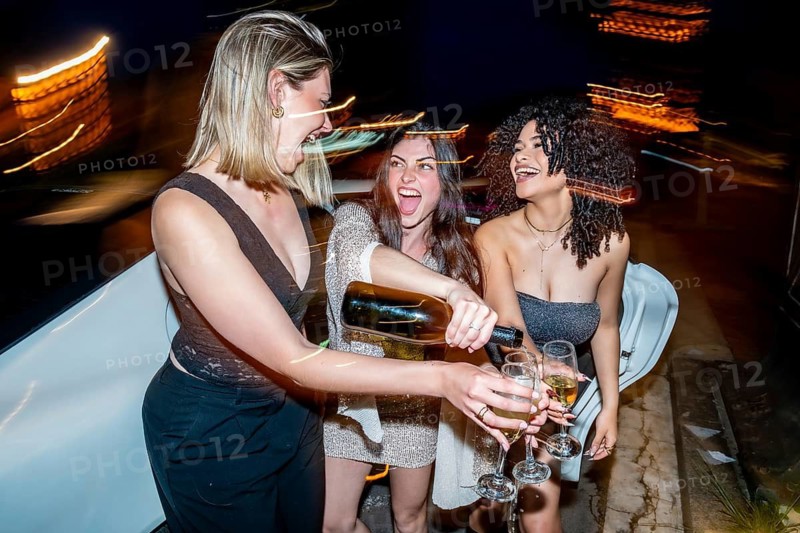 Young women enjoying a limousine party at night, pouring champagne into glasses and laughing together, conveying feelings of joy, friendship, and celebration during a luxury nightlife event