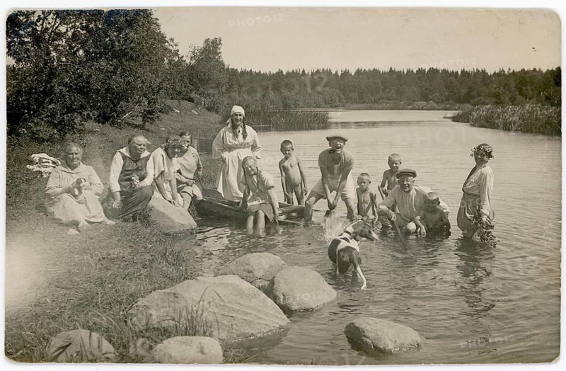 A group of people wearing traditional clothes enjoy a day at the river, accompanied by a dog. Historic flair and natural surroundings