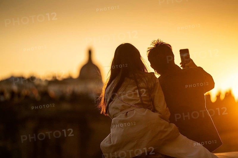 Young couple taking selfie at sunset, back light, urban landscape with dome in background, Florence, Tuscany, Italy