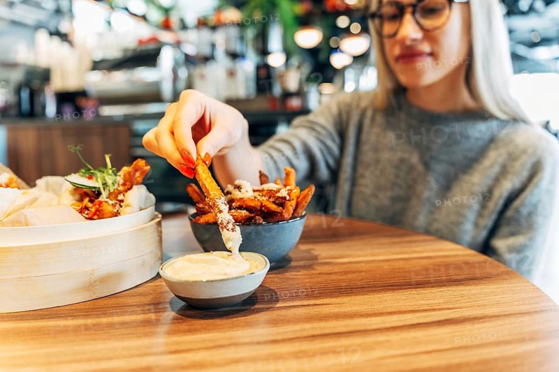 Young woman enjoying sweet potato fries with dip in a trendy urban cafe