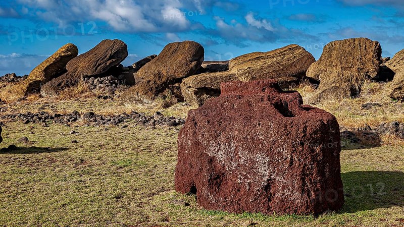 Large reddish stone in front of fallen Moai statues and a cloudy sky, The Moai Statues on Easter Island in the Pacific Ocean