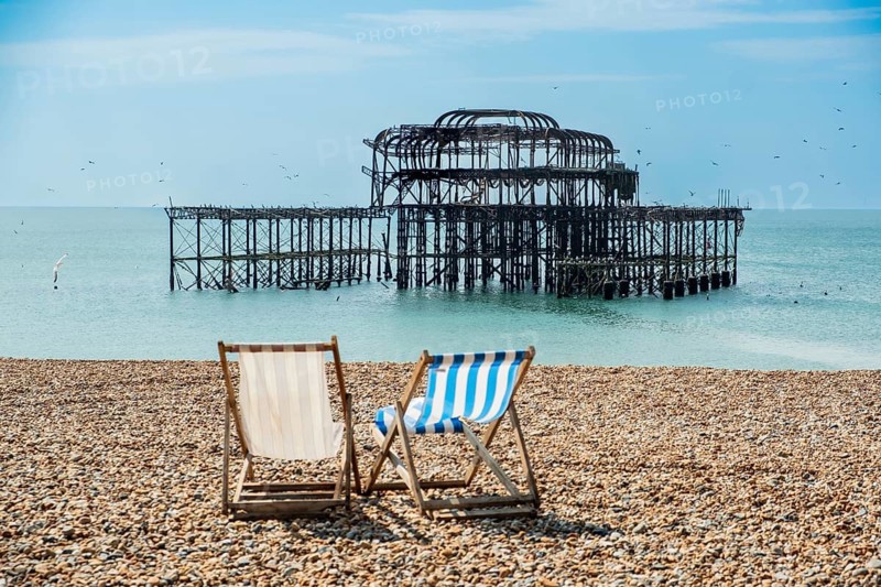Two folding chairs on the beach in front of the ruins of the burnt down West Pier in Brighton, East Sussex, England, Great Britain