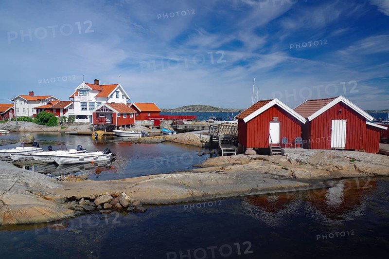 Red wooden houses on rocky coast, boats in calm water, picture under a cloudy sky, archipelago, Käringön, Västra Götalands län, Sweden