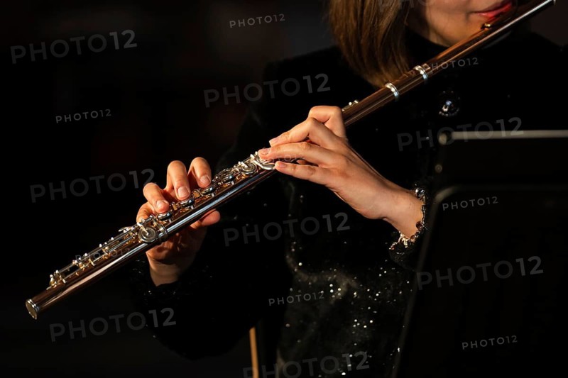 A detailed close-up shot of a female flutist's hands playing the keys of a silver transverse flute, showing intricate finger placement during a performance in Lubin, Poland
