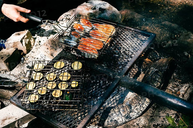 Cooking food on the grill during a picnic in the woods. Salmon steaks and sliced zucchini are grilled over a campfire