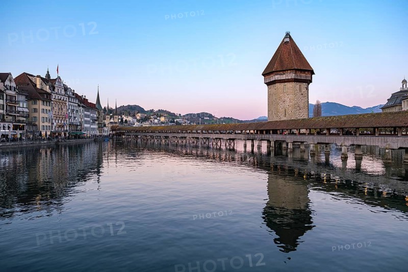 Historic wooden bridge and water tower in Lucerne at dusk with calming reflection in the water and mountains in the background, Chapel Bridge, Lucerne, Switzerland
