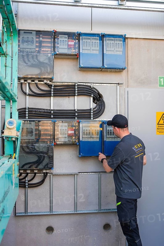 An electrician works on a control panel in a concrete technology room with exposed cables and terminals, electrical system for PV system, industrial customers, Mühlacker, Germany