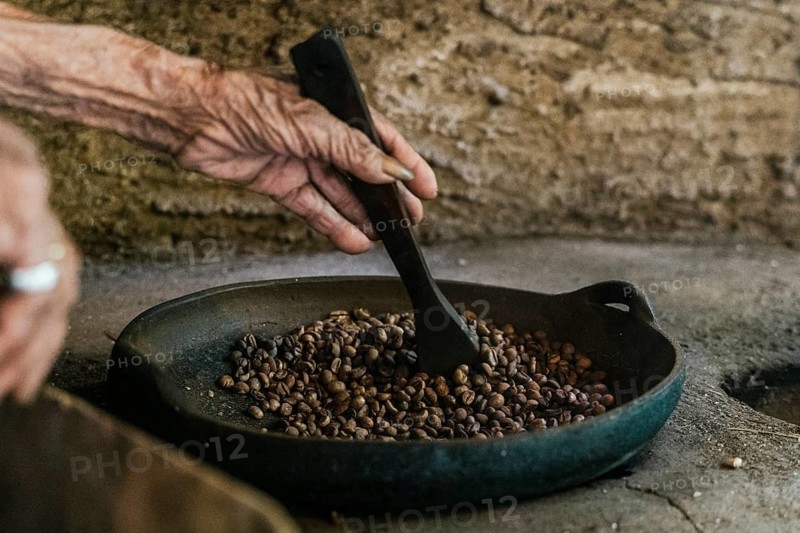 An elderly hand stirs balinese coffee beans in a pan, capturing the essence of traditional roasting methods in a rustic environment, highlighting cultural craftsmanship of Bali