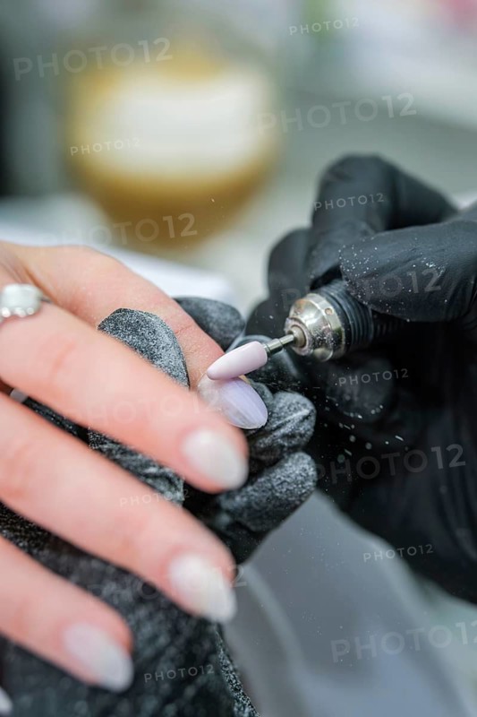 Precision manicure image of a rotating nail drill shaping the surface of a long almond nail while dust gathers on gloved hands