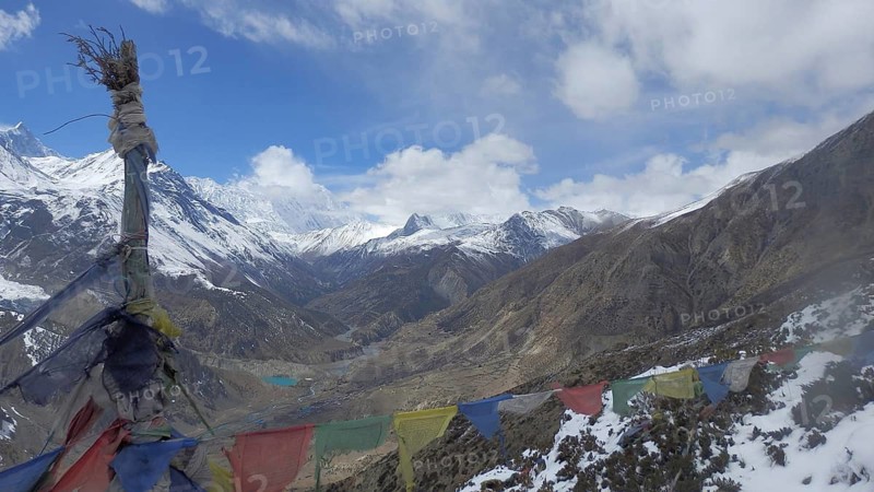 Wide mountain landscape with colorful prayer flags and snow-capped peaks under blue sky, trekking at Annapurna Circuit, Manang, Nepal