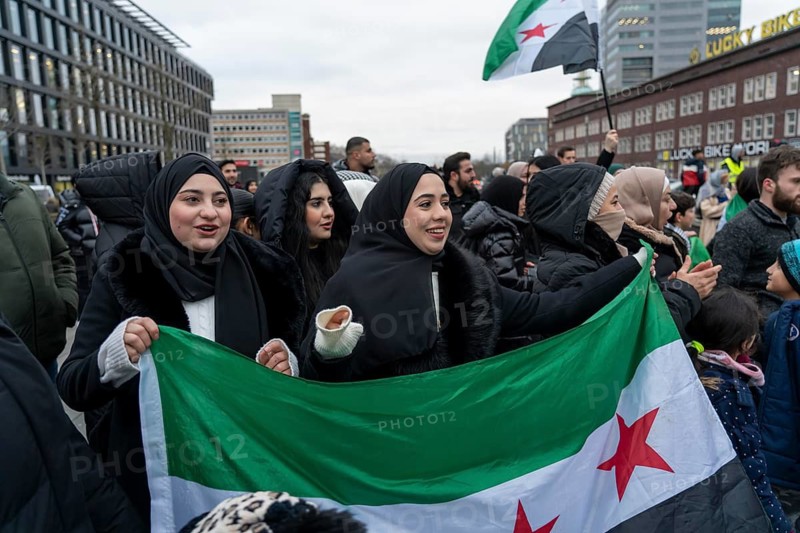 Syrian woman celebrate the end of the Assad regime after the change of power in Syria at a rally on the square in front of the main railway station in Duisburg, North Rhine-Westphalia, Germany