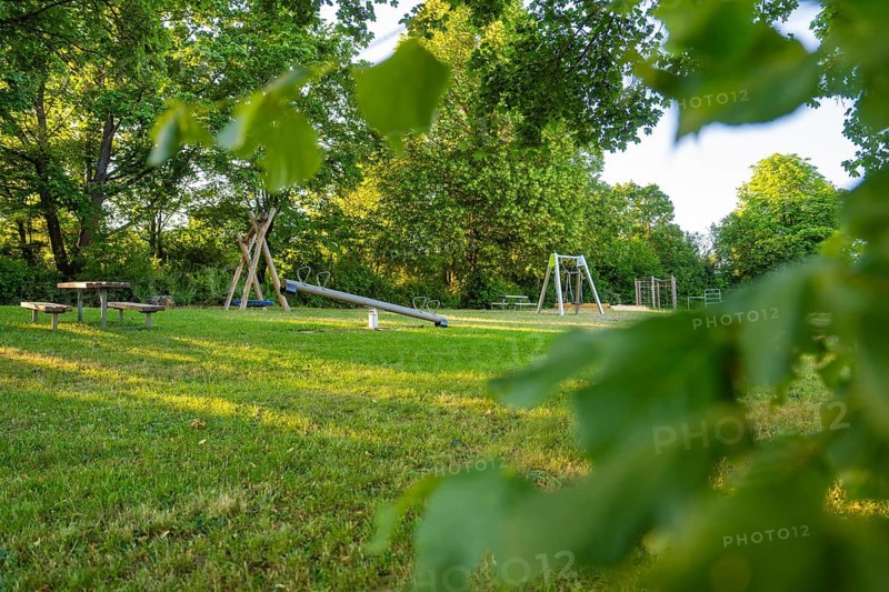 A playground with a seesaw on a green field surrounded by thick trees, Gechingen playgrounds, Calw district, Germany