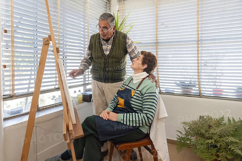 Senior couple sharing a cheerful conversation beside an easel in a bright home art studio