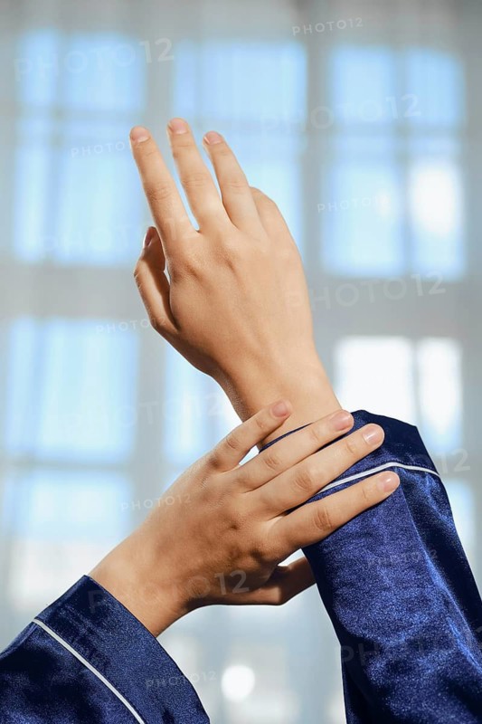 Two hands wearing blue clothing show gesture against a window with light coming through during daytime. Hands are positioned with fingers raised and bent