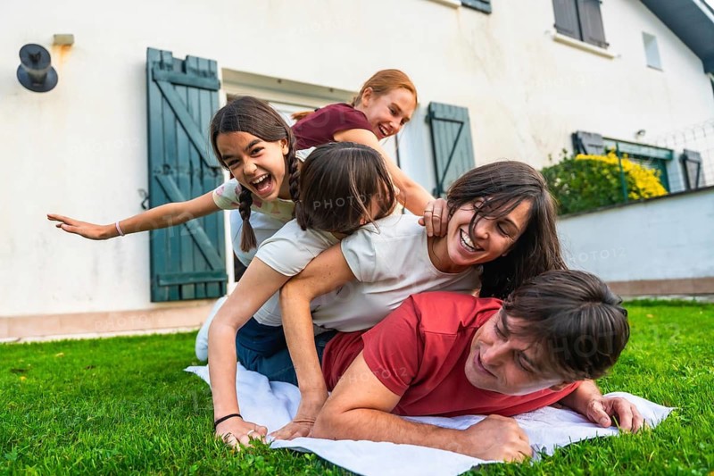 Cheerful parents and diverse children creating a human pyramid on green grass, enjoying playful summer activity and family bonding time together outdoors