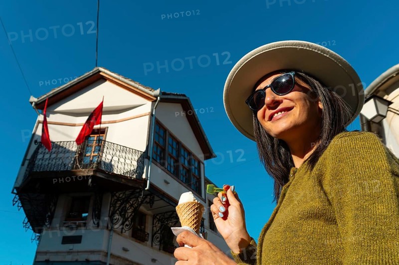 Close up happy woman smile enjoys traditional tasty vanilla ice cream while taking selfie at historic Zekate House in Gjirokastra, Albania. UNESCO 19th-century Ottoman architecture and stone roofs