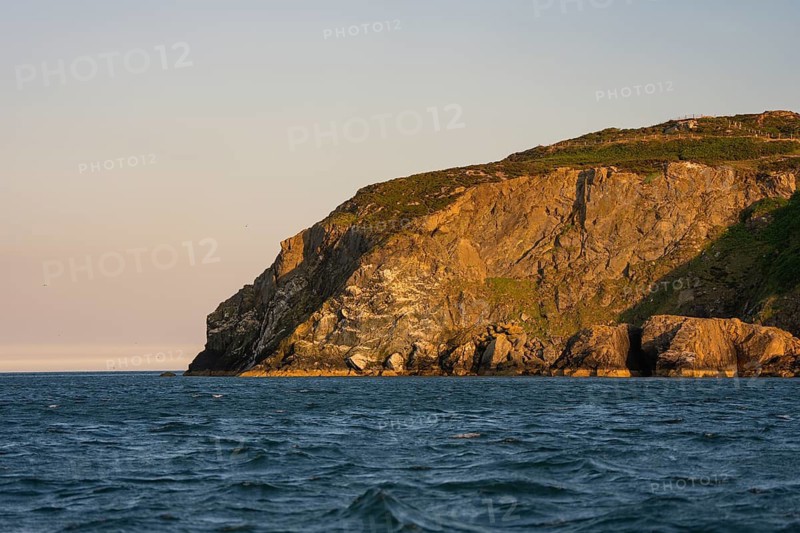 Rocky cliffs jutting into the illuminated evening sea at calm seas, Howth, Ireland