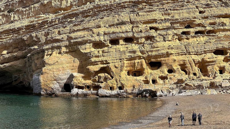 Rock formation with caves on the edge of a beach, small group of people on the shore, Matala, Neolithic caves, former hippie paradise, central south coast, Crete, Greek Islands, Greece