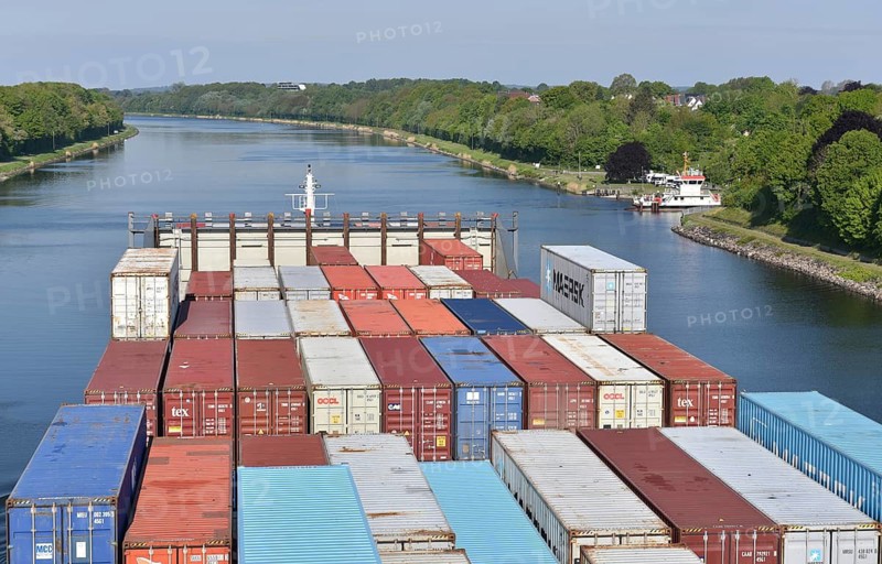 Giant container ship transports containers on river, green landscape, blue sky, container ship sails through the Kiel Canal, NOK, Kiel Canal, Kiel Canal, Schleswig-Holstein, Germany