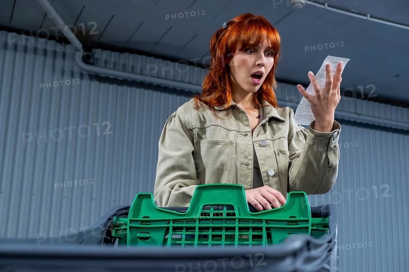 Young woman shocking holding a grocery store receipt, looking at the high total price and experiencing financial stress and concern about inflation and the cost of living crisis while shopping