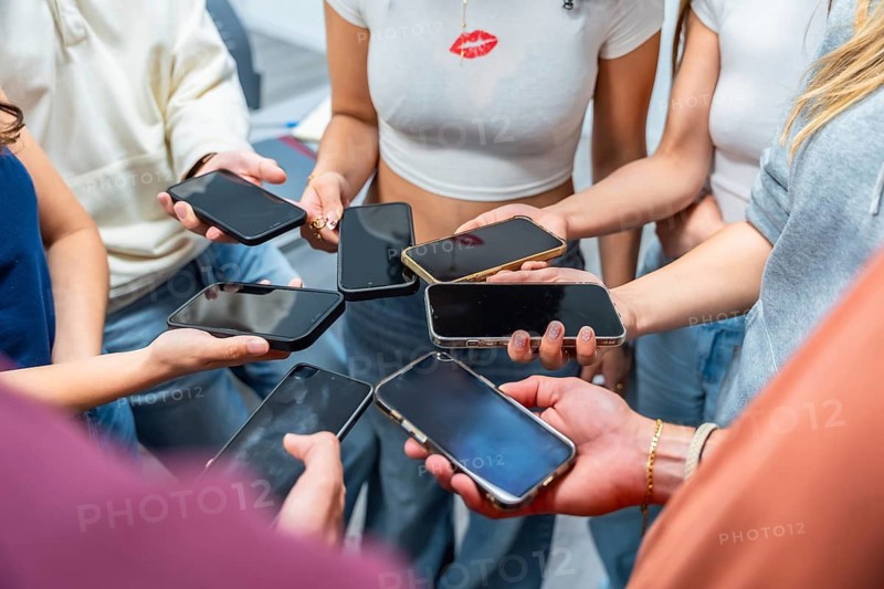 Teenagers are holding many mobile phones, forming a circle with their hands and connecting through technology and social media in a digital world context