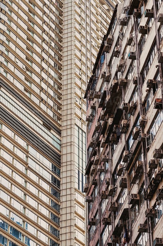 High contrast view of modern and aged architectural styles in Hong Kong, showcasing the diversity in building designs and conditions. The image captures both sleek, clean lines and weathered structures with external air conditioners
