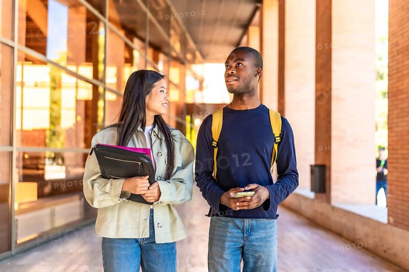 Two african and chinese multi-ethnic exchange students arriving at the university walking and talking together