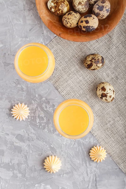 Sweet egg liqueur in glass with quail eggs and meringues on a gray concrete background. Top view, close up, flat lay