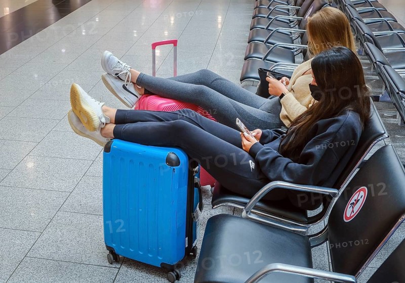 Düsseldorf, North Rhine-Westphalia, Germany - Düsseldorf Airport, start of the holidays in North Rhine-Westphalia, young woman sitting in the departure hall, their legs relaxed on their suitcases, waiting to take off on their summer holidays in times of the corona pandemic