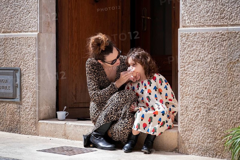 A tender moment captured between a mother and her daughter sitting on steps outside their village home. The mother lovingly tends to her child, creating a warm family scene