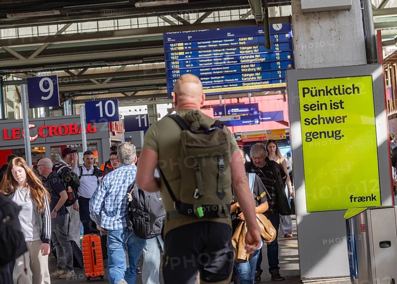 Being on time is hard enough. Advertising for the Fränk mobile app in Stuttgart Central Station. People on the platform. Stuttgart, Baden-Württemberg, Germany