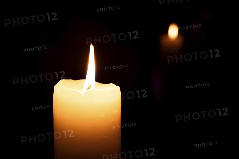 Lit candle in the dark and its reflection in the background