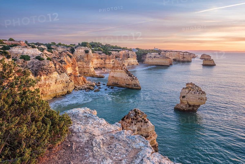 Sunrise view of Praia da Marinha beach in Algarve, Portugal, with a limestone sea arch, Atlantic water, warm sky, and rugged coastal cliffs