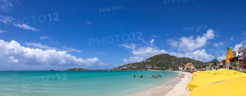 Wide panoramic view of the beach at Great Bay in Philipsburg Sint Maarten featuring numerous yellow umbrellas turquoise water and a green mountain coastline