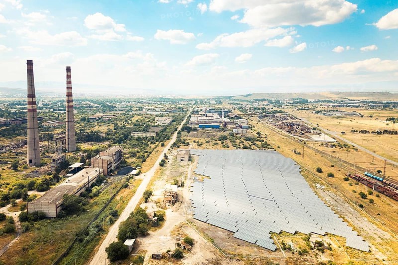 Aerial fly over view of solar power plant or farm next to abandoned industrial complex in Rustavi Georgia illustrating contrast of renewable energy progress and decaying polluting heritage