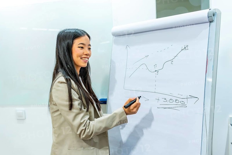 Young asian businesswoman drawing positive growth chart on flip chart during a presentation in coworking office