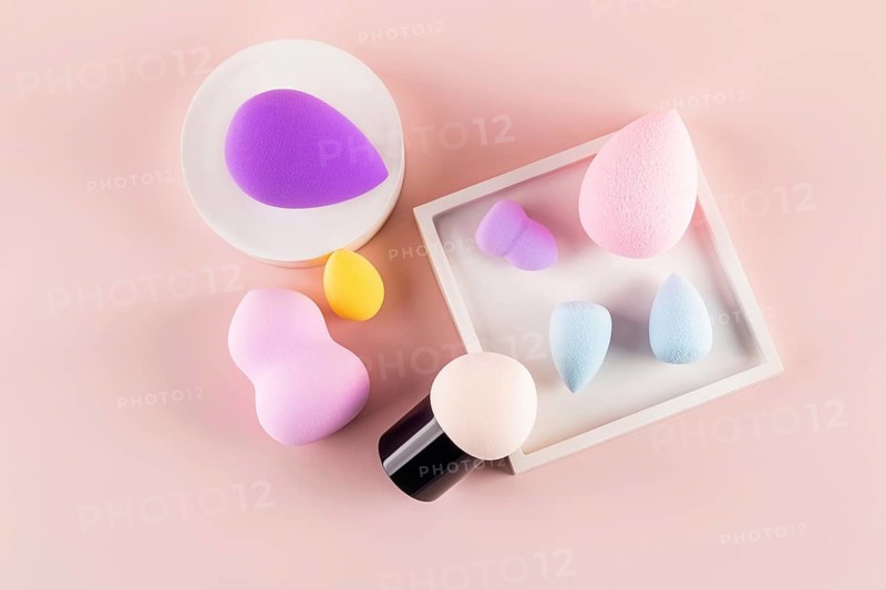 Top view of assorted makeup sponges, including a beauty blender, arranged on a pink background, demonstrating diversity in beauty tools