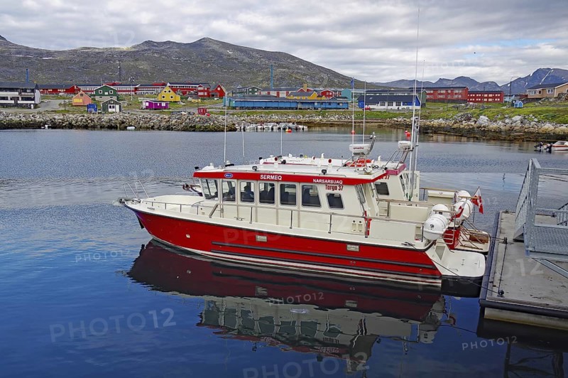 Red boat in the harbour with colourful houses in the background and mountains under a cloudy sky, passenger ferry, Narsarsuaq, Greenland, Denmark