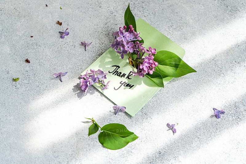 An elegant thank you card adorned with vibrant lilac flowers and green leaves lies on a textured surface, capturing the essence of gratitude and nature beauty