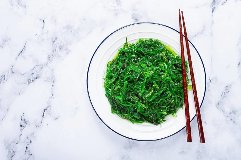 Chuka salad, made from fresh seaweed, with sesame dressing, served on a white plate, with chopsticks, no people