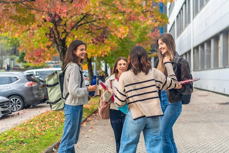 Group of happy female university students standing together and enjoying conversation on a college campus during autumn, surrounded by colorful foliage