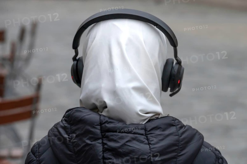 Young woman wearing headscarf and headphones in pedestrian zone, Bavaria, Germany