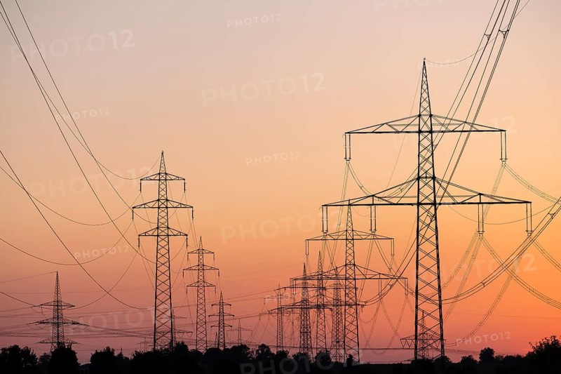 Silhouette of several high-voltage power lines and electricity pylons against a glowing orange and red sunset sky in Germany