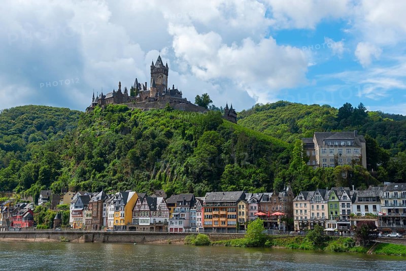 Castle on a wooded hill with colourful buildings along a river, clouds in the sky below, Reichsburg, Cochem, Cochem-Zell, Moselle, Rhineland-Palatinate, Germany