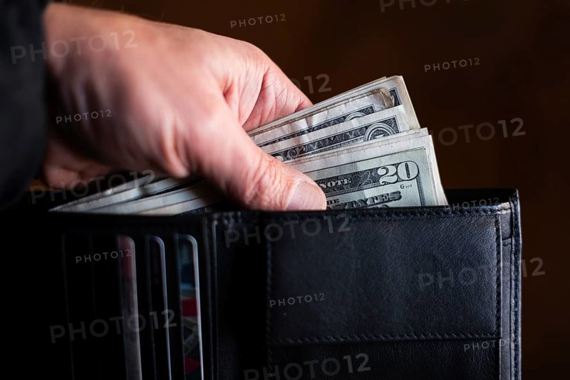 A blurred hand places or taking folded US dollar bills, with 20$ banknote visible, into a dark wallet. Concepts of savings, payment, budget, and finance in Poland