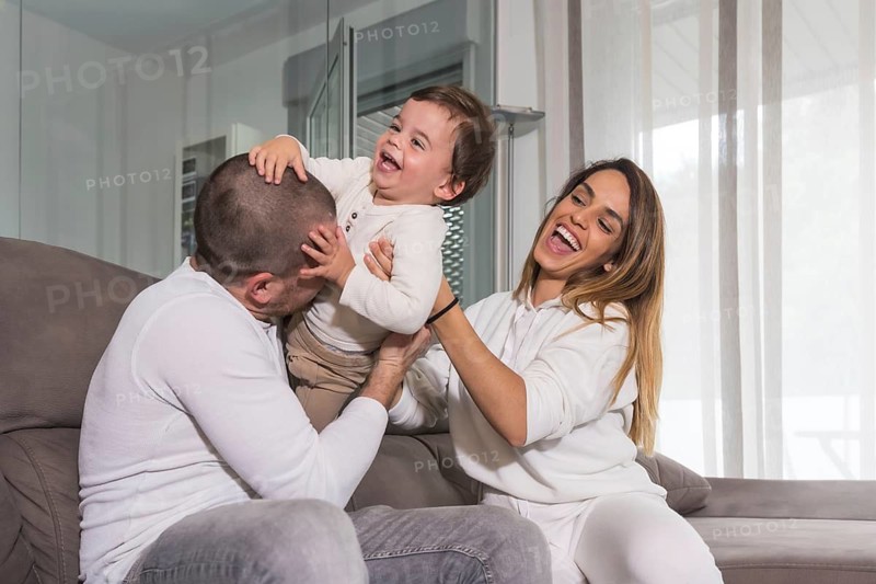 Happy family laughing and playing on the sofa with their baby