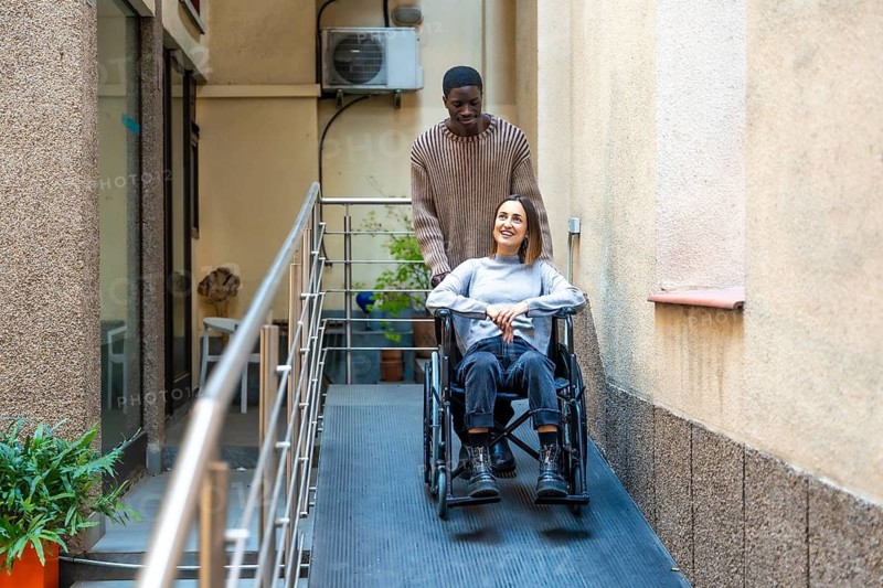 African man pushing the wheelchair of disabled colleague leaving a modern coworking building